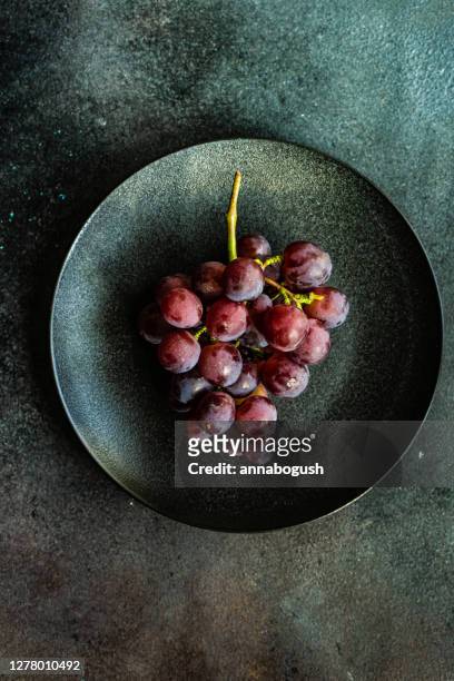overhead view of a bunch of red grapes on a ceramic plate - red grapes stock-fotos und bilder