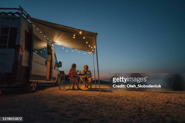 pareja cerca de la caravana estacionada cerca del mar al atardecer - camping de lujo fotografías e imágenes de stock