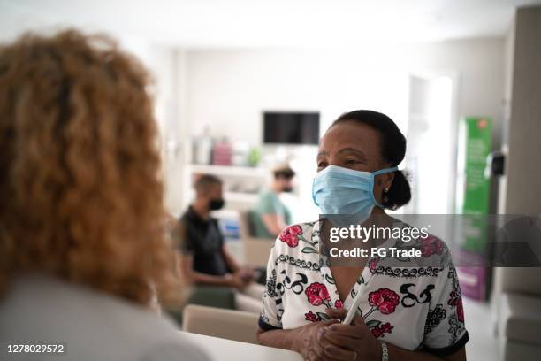 medical clinic reception, patient waiting in line respecting social distancing using face mask - crowd masks stock pictures, royalty-free photos & images