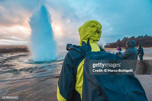 photographer admiring the eruption of a geyser in iceland - geothermie gebiet stock-fotos und bilder