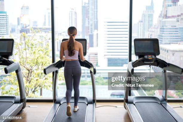 rear view of fitness woman running on treadmill during a cardio session against city view in a health club. - トレッドミル　女性 ストックフォトと画像