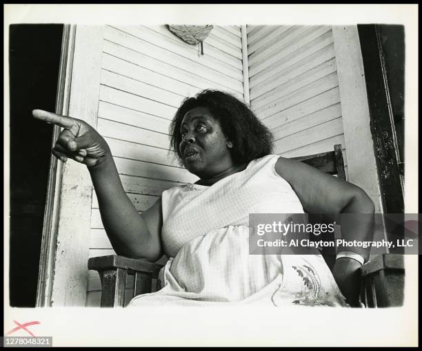 African American Activist, Fannie Lou Hamer, sitting on porch in white dress, pointing finger. Shot from waist up in Ruleville, Mississippi 1969....