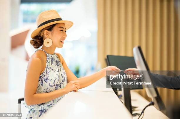 side view of young asian women traveler, check in or paying at front desk. her receiving a hotel room key from customer service representative. - ホテルマン ストックフォトと画像