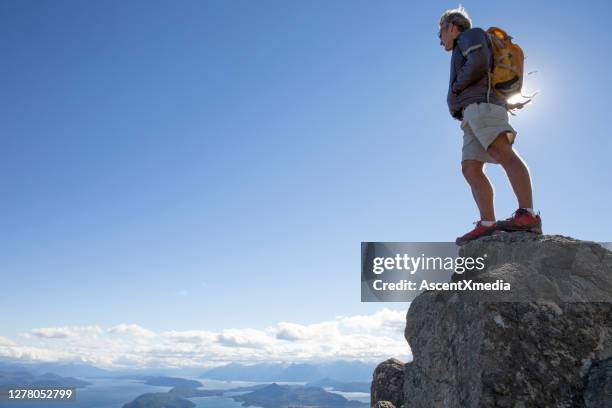 male hiker ascends steep rock bluff, above mountains and lake - bariloche argentina stock pictures, royalty-free photos & images