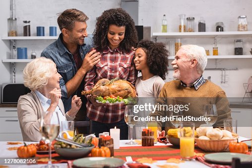 Selective focus of african american woman holding turkey near family during thanksgiving celebration Selective focus of african american woman holding turkey near family during thanksgiving celebration