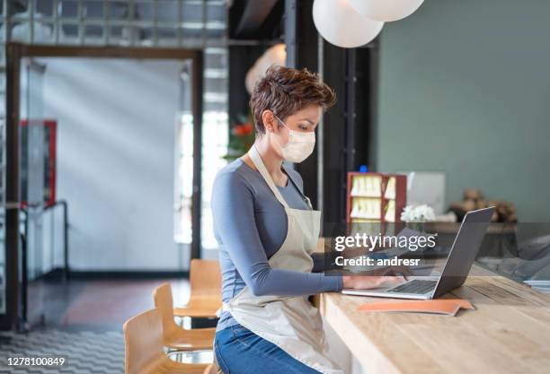 business owner wearing a facemask while bookkeeping at a restaurant - business plan covid stock pictures, royalty-free photos & images