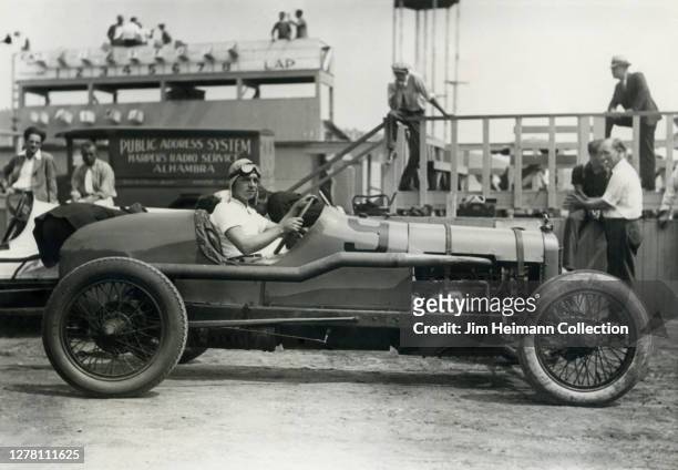 Joe Crocker poses in a race car at the speedway with a group of spectators milling about in the background, circa 1935.