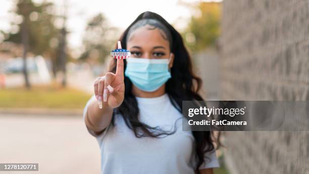 young woman holds up "i voted" sticker - voting mask stock pictures, royalty-free photos & images