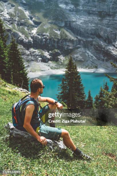 man sitting on the grass while enjoying the view of oeschinensee - kandersteg stock pictures, royalty-free photos & images