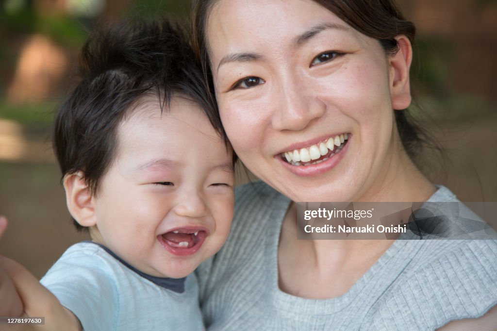 A baby hugged by a young mother and smiling