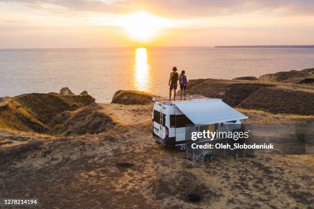 aerial view of heterosexual couple on roof of camper van on seaside  at sunset - rural couple young stock pictures, royalty-free photos & images