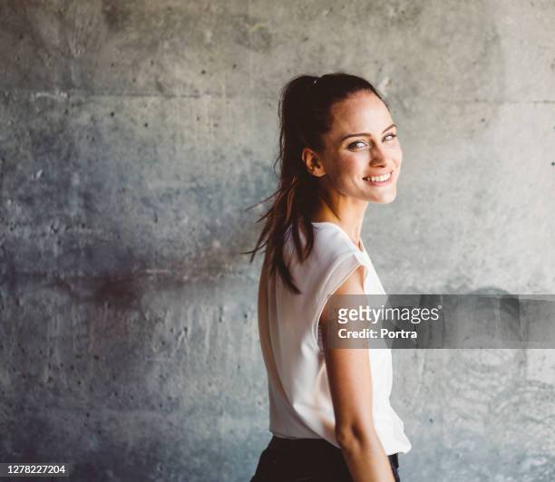 ritratto di giovane donna sorridente da parete grigia - tre quarti foto e immagini stock