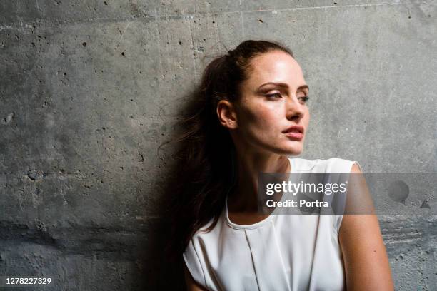 thoughtful woman looking away while day dreaming - concrete wall stock pictures, royalty-free photos & images