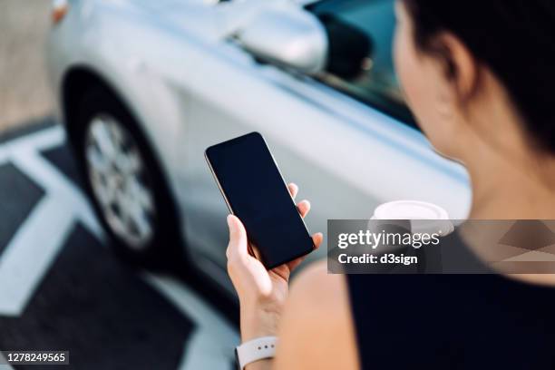 over the shoulder view of confidence and professional young asian businesswoman walking to her car, using smartphone and holding a cup of coffee. business on the go concept - management car smartphone stock pictures, royalty-free photos & images