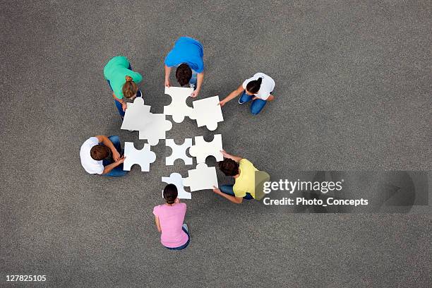 people putting together jigsaw puzzle - groep objecten stockfoto's en -beelden