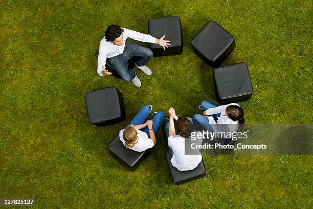 people talking in circle in grass - teambuilding stockfoto's en -beelden