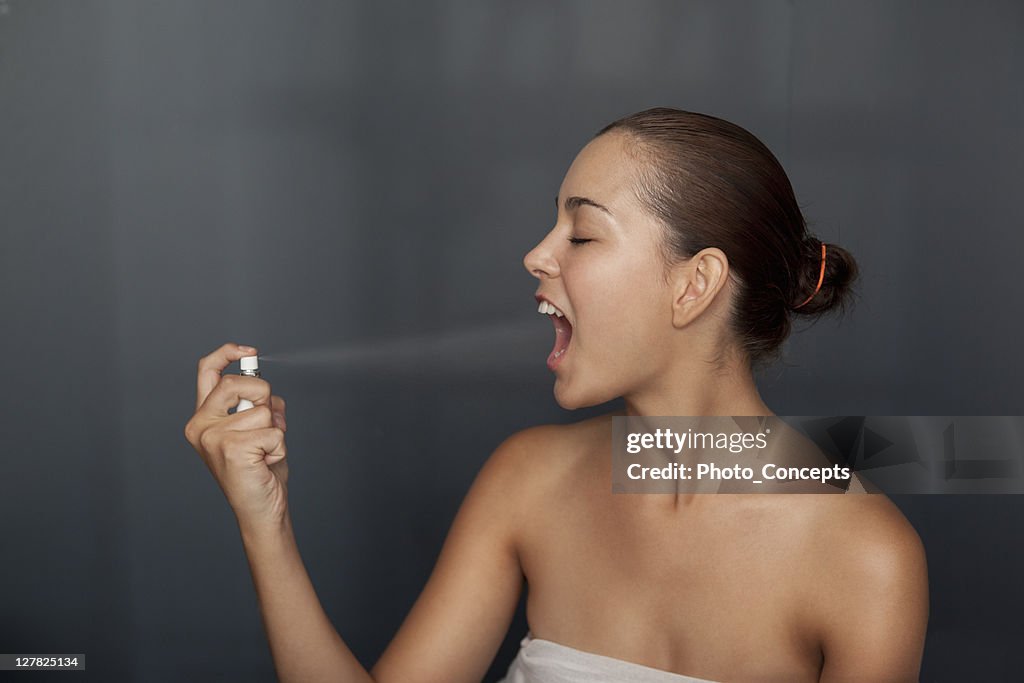 Mulher de aspersão spray de respiração na sua boca.