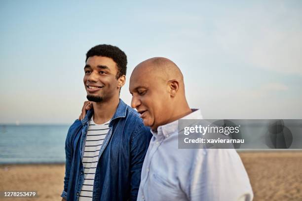 pai afetuoso caminhando na praia com filho adulto jovem - filhos adultos - fotografias e filmes do acervo