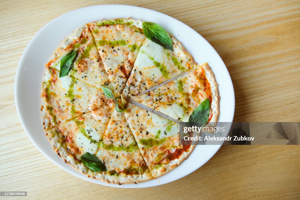 Hot Italian pizza Margarita or pesto with cheese in a cardboard box or packaging for delivery, on a ceramic plate in a cafe or pizzeria. Vegetarian food. Fast food.