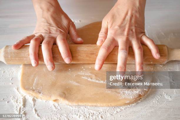 female hands housewife with wedding ring roll out dough wooden rolling pin on white table background - rolling pin stock-fotos und bilder