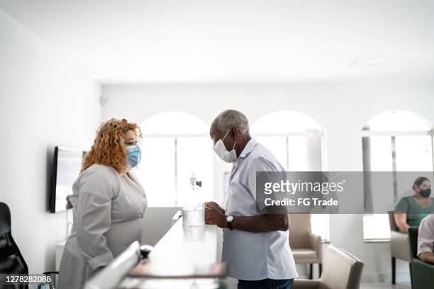 medical clinic reception, receptionist talking to patient using face mask - entering hospital stock pictures, royalty-free photos & images
