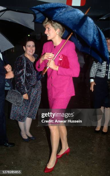Diana, Princess of Wales, wearing a pink suit with gold buttons designed by Paul Costelloe, holds an umbrella during a visit to Sudbury on October...
