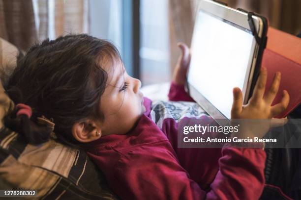 2 years old girl looking tablet at home - lying on back girl on the sofa imagens e fotografias de stock