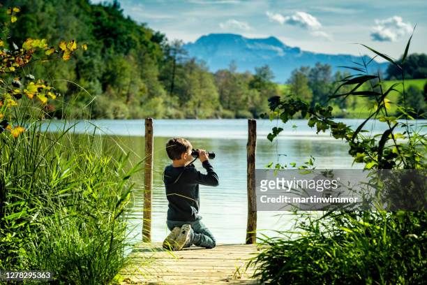 kleiner junge mit fernglas an einem holzsteg an einem österreichischen see - österreich durchblick stock-fotos und bilder