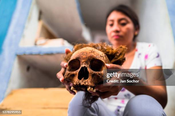 Young Mayan woman holds a dried-up scull of her deceased grandmother during the bone cleansing ritual at the cemetery on October 27, 2019 in Pomuch,...