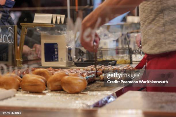 selective focus, heap of grilling sausages on barbecue grill beside brötchen, german style bread, at a stall of christmas market in winter season in germany. - hot dog stand stockfoto's en -beelden