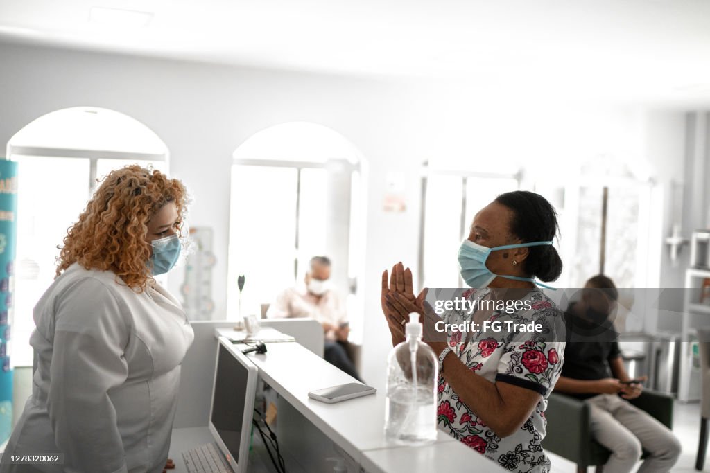 Patient arriving at medical clinic reception and using hand sanitizer using face mask