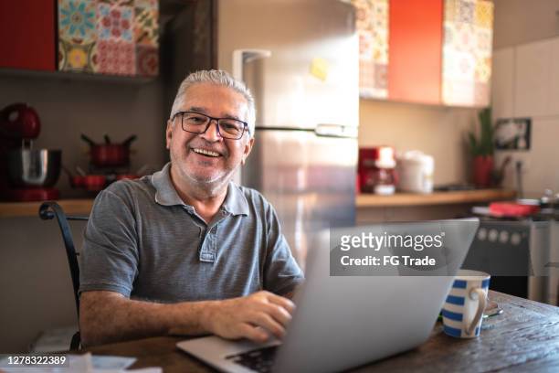 portrait of senior man using laptop at home - senior men computer stock pictures, royalty-free photos & images