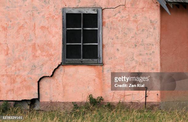 big crack on an old wall of a pink painted building that runs from ground to a window - abandoned crack house stock pictures, royalty-free photos & images