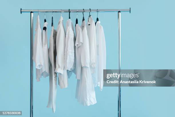 close-up of white clothes hanging on rack on blue background. - clothes wardrobe stock-fotos und bilder