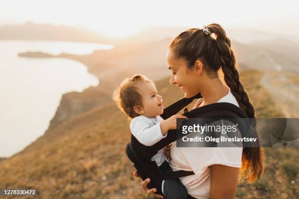 woman travel and hike with toddler baby in sling. active lifestyle - marsupio foto e immagini stock