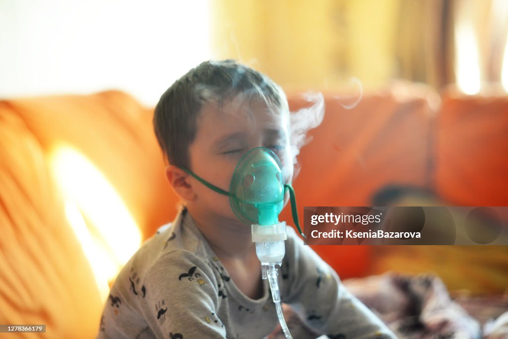 The boy breathes through the inhaler. The boy is being treated