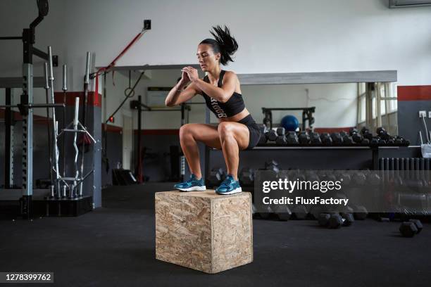 mujer joven y en forma saltando en una caja en el gimnasio - entrenamiento combinado fotografías e imágenes de stock