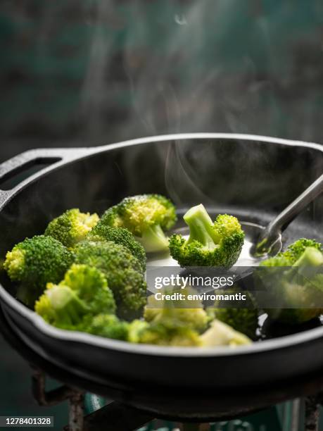 fresh broccoli spears being sauteed/stir fried in a heavy iron pan on a gas stove against a turquoise colored background. - saute stock pictures, royalty-free photos & images