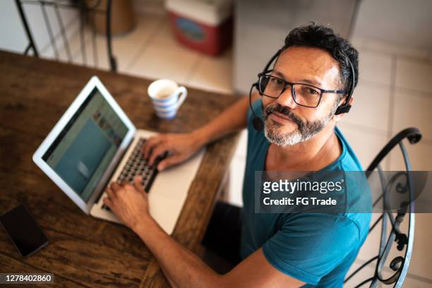 ritratto di un uomo maturo che lavora da casa, indossa cuffie e usa il laptop - solo un uomo maturo foto e immagini stock