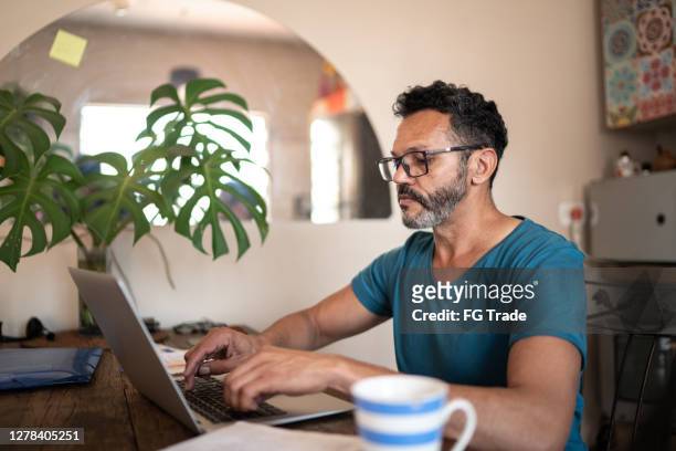 reife mann mit laptop zu hause arbeiten - männer über 40 stock-fotos und bilder
