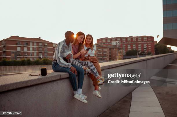 three female friends sitting and using a mobile phone - music speaker stock pictures, royalty-free photos & images