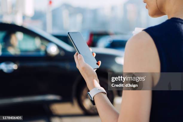 over the shoulder view of young asian businesswoman using mobile app device on smartphone to arrange a taxi pick up service in the city. speedy and trustworthy service. crowdsourcing and business on the go concept - carsharing stock pictures, royalty-free photos & images