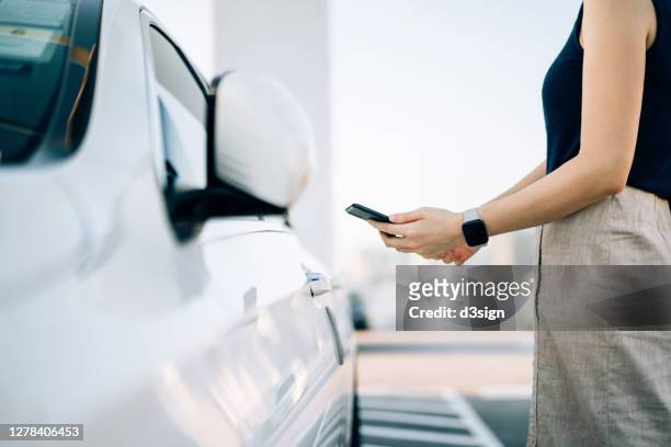 close up of young asian woman using mobile app device on smartphone to unlock the doors of her car in a car park - coche futurista fotografías e imágenes de stock
