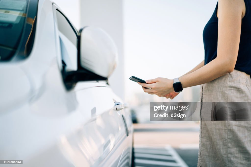 Close up of young Asian woman using mobile app device on smartphone to unlock the doors of her car in a car park