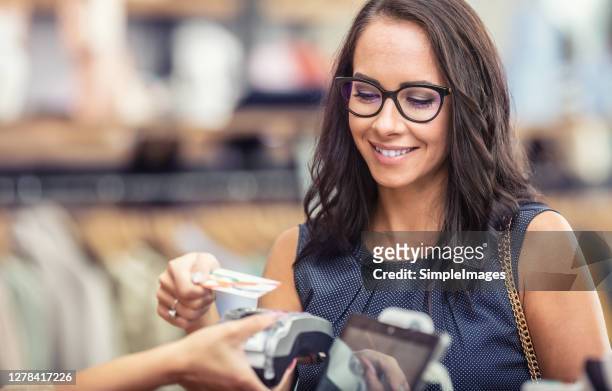 contactless payment by a credit card in the store by a brunette in glasses. - customers pay with contactless cards imagens e fotografias de stock