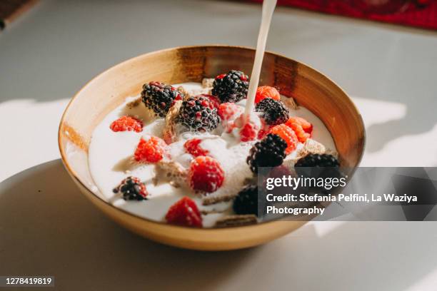 dairy free milk pouring into a bowl of whole grain cereal, raspberries and blackberries. - pouring softdrink stock-fotos und bilder