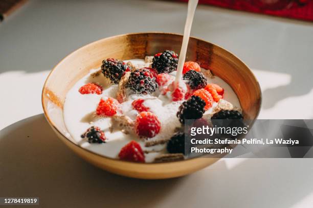 dairy free milk pouring into a bowl of whole grain cereal, raspberries and blackberries. - oat milk stock pictures, royalty-free photos & images