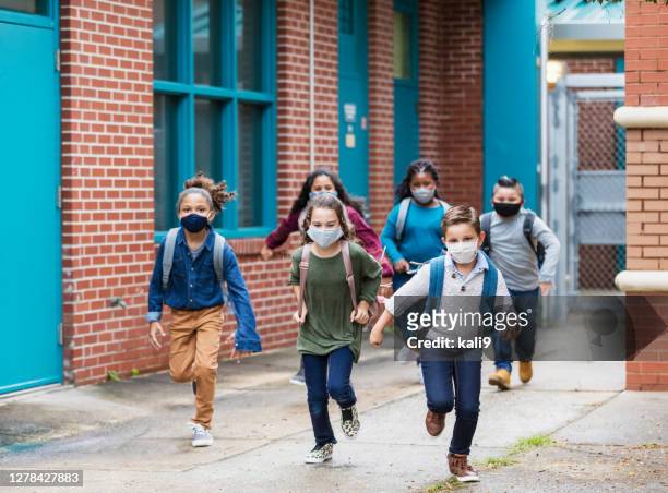 bambini delle scuole con maschere per il viso che corrono fuori dall'edificio - educazione foto e immagini stock