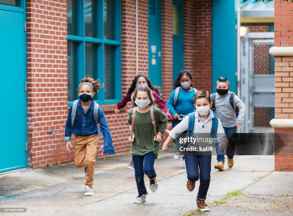 School children with face masks running outside building