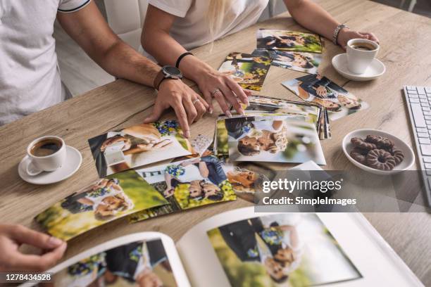 married couple look at their printed wedding photos spread across the table, having a coffee. - memorial day background fotografías e imágenes de stock